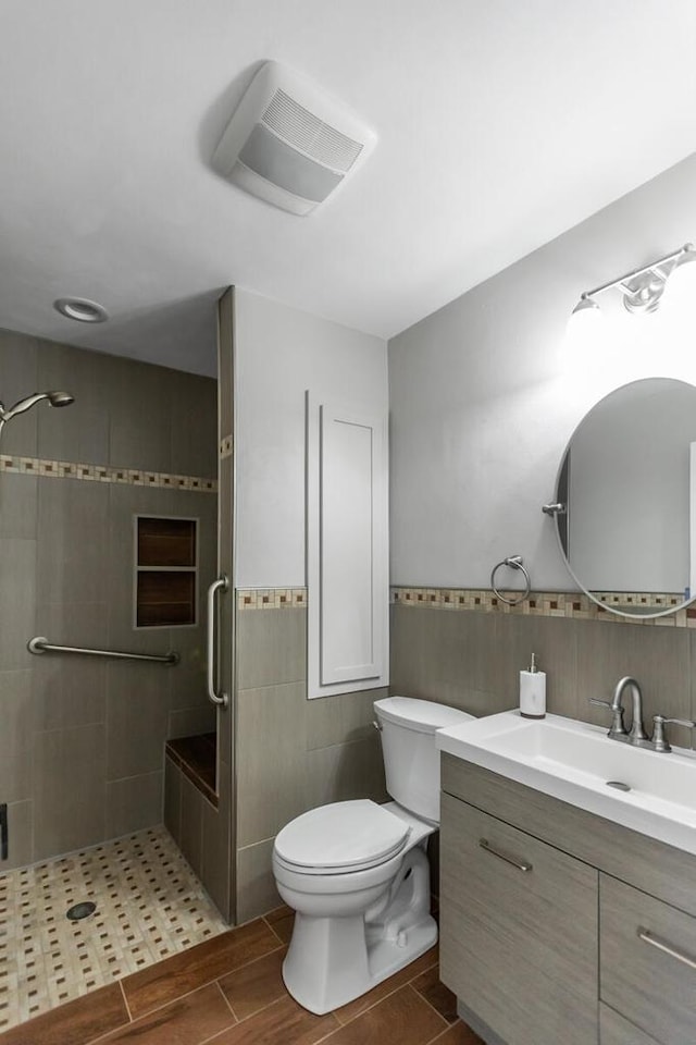 bathroom with a tile shower, vanity, toilet, and tile walls