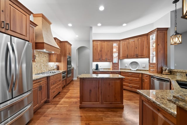 kitchen featuring decorative light fixtures, custom exhaust hood, hardwood / wood-style flooring, stainless steel appliances, and light stone countertops