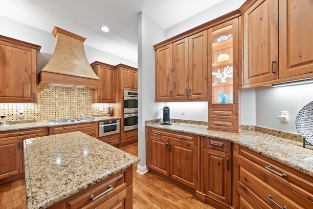 kitchen with light stone counters, tasteful backsplash, stainless steel appliances, and custom range hood