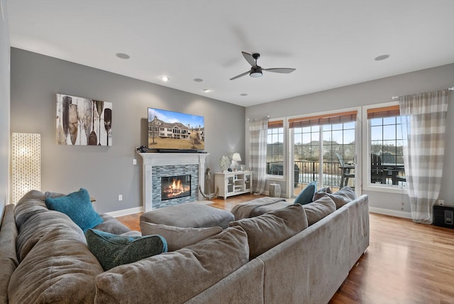 living room with a stone fireplace, hardwood / wood-style floors, and ceiling fan