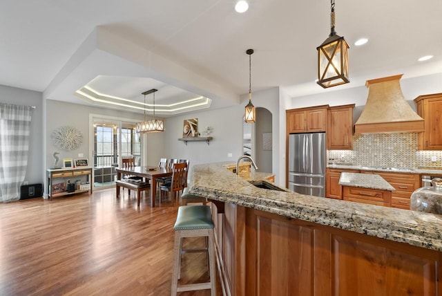 kitchen featuring light hardwood / wood-style flooring, stainless steel refrigerator, hanging light fixtures, a tray ceiling, and custom range hood