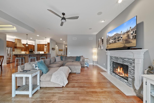 living room with ceiling fan, a fireplace, and light wood-type flooring