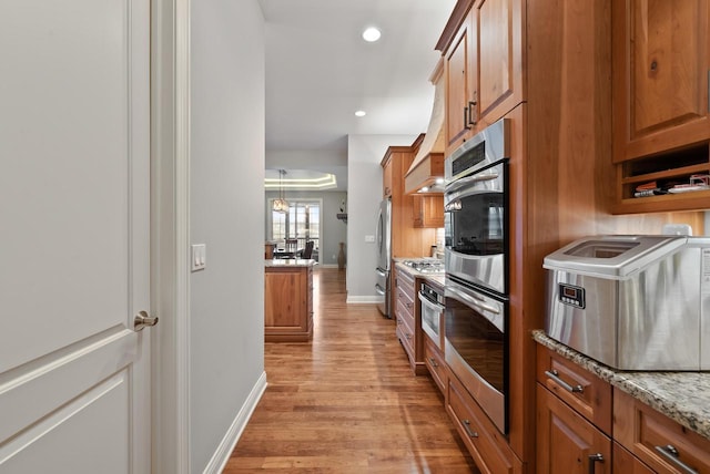 kitchen with light hardwood / wood-style floors, light stone countertops, and stainless steel refrigerator