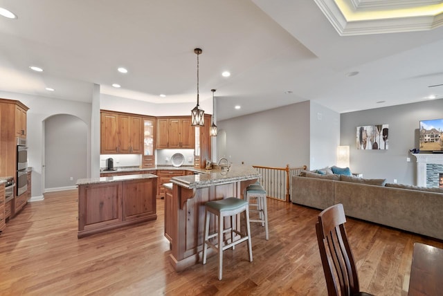 kitchen with hanging light fixtures, light stone countertops, kitchen peninsula, and light wood-type flooring