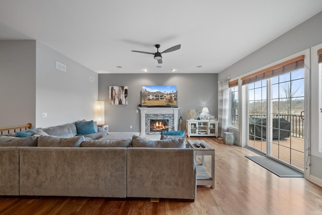 living room featuring ceiling fan, a fireplace, and light wood-type flooring