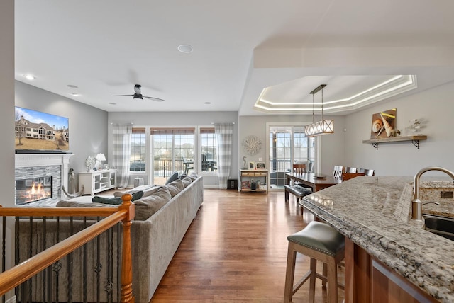 living room with dark wood-type flooring, sink, a raised ceiling, ceiling fan, and a fireplace