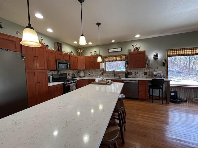 kitchen featuring a breakfast bar, stainless steel appliances, hanging light fixtures, dark wood-type flooring, and a sink