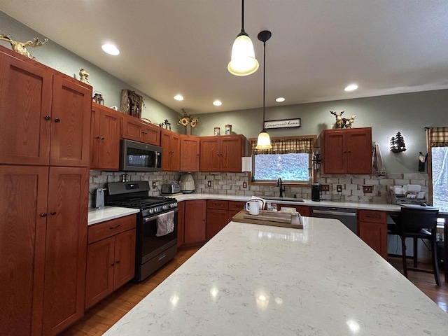 kitchen featuring light stone counters, a sink, hanging light fixtures, appliances with stainless steel finishes, and decorative backsplash