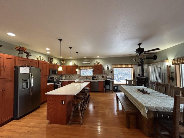 kitchen with stainless steel appliances, a wood stove, light countertops, a center island, and decorative light fixtures