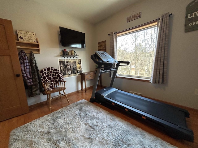 exercise area featuring lofted ceiling, baseboards, and wood finished floors