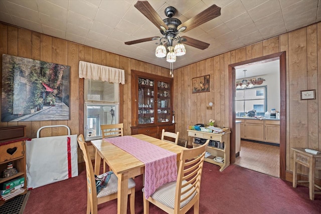 dining area featuring dark colored carpet, ceiling fan, and wood walls