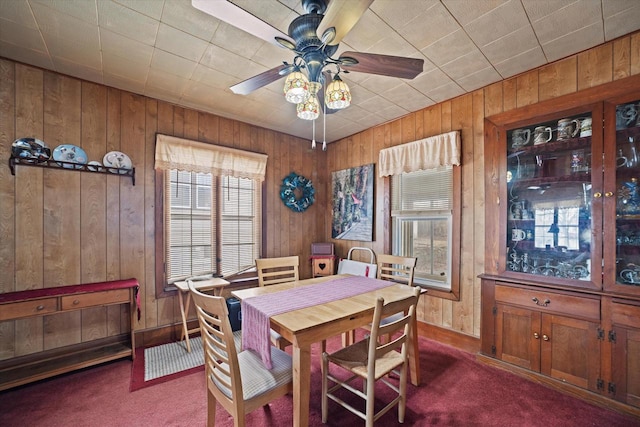 carpeted dining space with wooden walls and ceiling fan