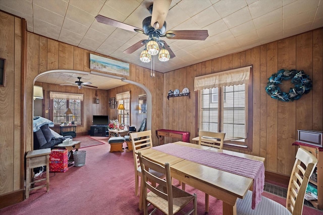 dining area featuring wood walls, ceiling fan, and carpet flooring