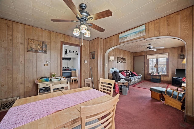 dining area with wooden walls, ceiling fan, and carpet