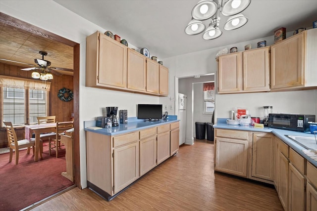 kitchen with white refrigerator, light hardwood / wood-style floors, light brown cabinets, ceiling fan with notable chandelier, and wood walls