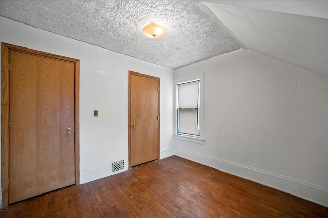 unfurnished bedroom featuring dark hardwood / wood-style flooring, vaulted ceiling, and a textured ceiling