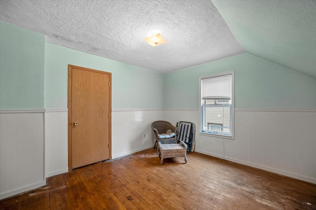 unfurnished room featuring lofted ceiling, hardwood / wood-style floors, and a textured ceiling