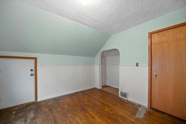 additional living space featuring hardwood / wood-style flooring, vaulted ceiling, and a textured ceiling