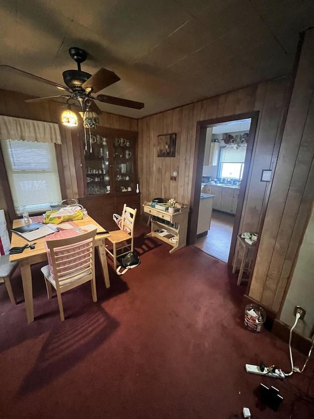 carpeted dining space with wooden walls and ceiling fan