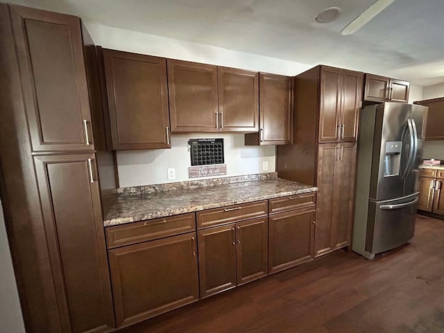 kitchen with dark stone countertops, stainless steel fridge with ice dispenser, dark brown cabinets, and dark hardwood / wood-style floors