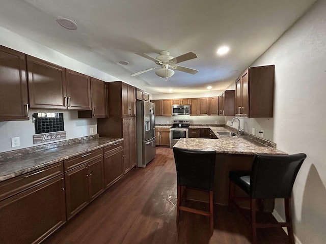 kitchen with sink, dark wood-type flooring, ceiling fan, stainless steel appliances, and a kitchen bar