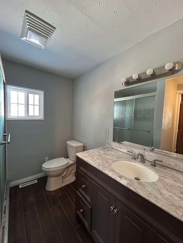 bathroom featuring vanity, toilet, a shower with door, and a textured ceiling