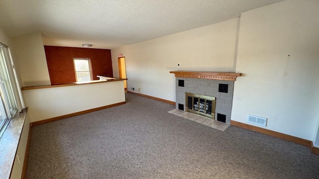 unfurnished living room with a tiled fireplace, light carpet, and a textured ceiling