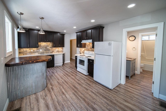 kitchen featuring under cabinet range hood, white appliances, wood finished floors, a sink, and decorative light fixtures