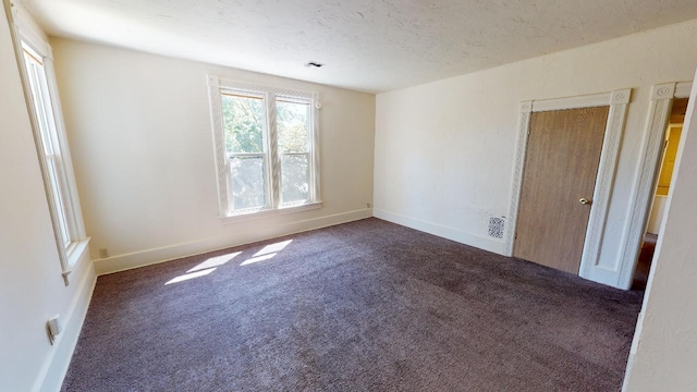 empty room with a textured ceiling, dark carpet, visible vents, and baseboards