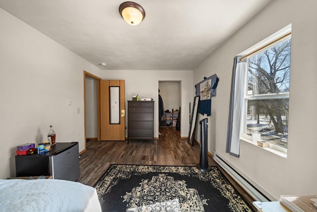 bedroom with a baseboard heating unit, dark wood finished floors, freestanding refrigerator, and baseboards