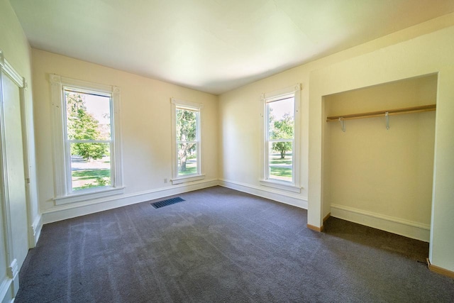 unfurnished bedroom featuring baseboards, visible vents, dark carpet, and a closet