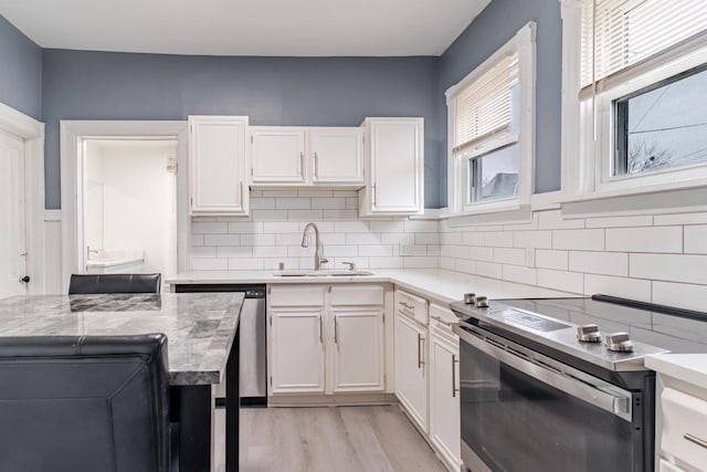 kitchen featuring sink, light hardwood / wood-style flooring, appliances with stainless steel finishes, white cabinets, and decorative backsplash