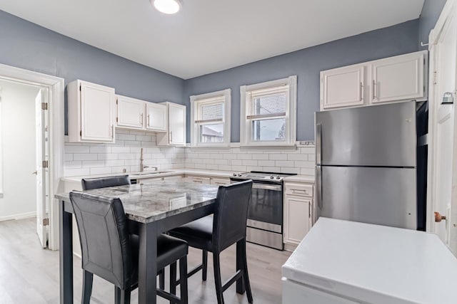 kitchen featuring sink, appliances with stainless steel finishes, white cabinetry, light stone countertops, and decorative backsplash