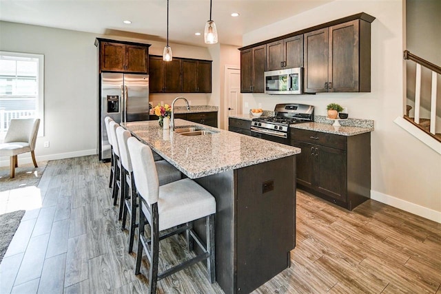 kitchen with decorative light fixtures, sink, stainless steel appliances, light stone countertops, and a center island with sink