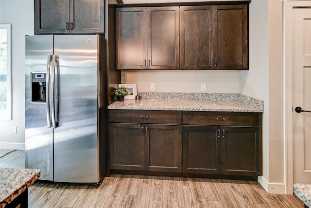 kitchen with stainless steel refrigerator with ice dispenser, dark brown cabinetry, light hardwood / wood-style floors, and light stone counters