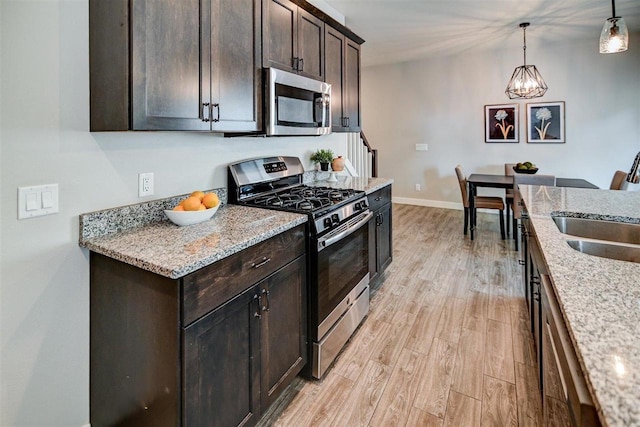 kitchen featuring stainless steel appliances, light stone countertops, pendant lighting, and dark brown cabinetry