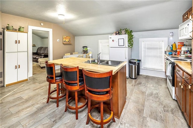 kitchen with sink, white appliances, an island with sink, a kitchen bar, and vaulted ceiling