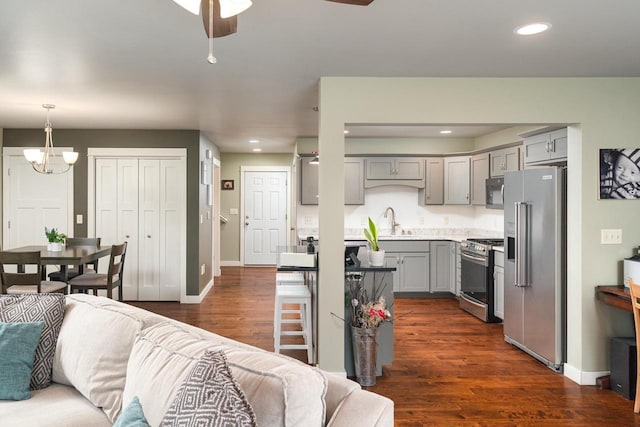 living room with dark wood-type flooring, ceiling fan with notable chandelier, and sink