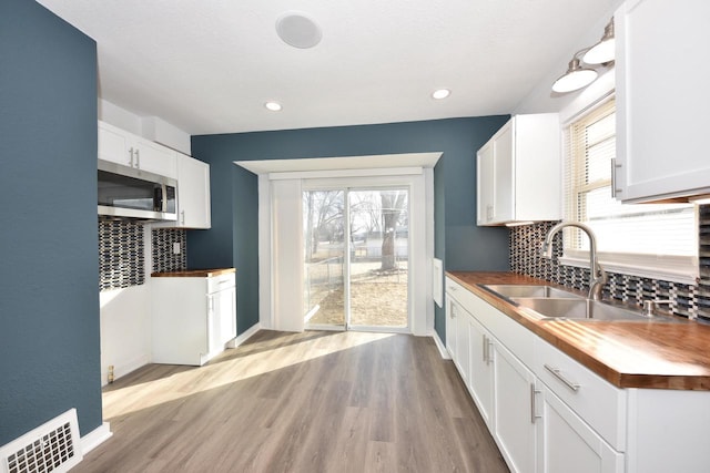 kitchen with sink, tasteful backsplash, wooden counters, light hardwood / wood-style flooring, and white cabinets