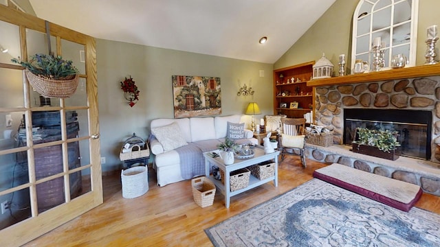 living room featuring hardwood / wood-style flooring, a stone fireplace, vaulted ceiling, and built in features