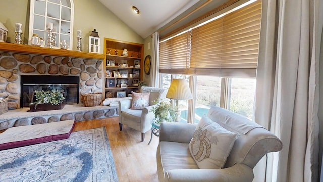 sitting room with built in features, a fireplace, vaulted ceiling, and light hardwood / wood-style flooring