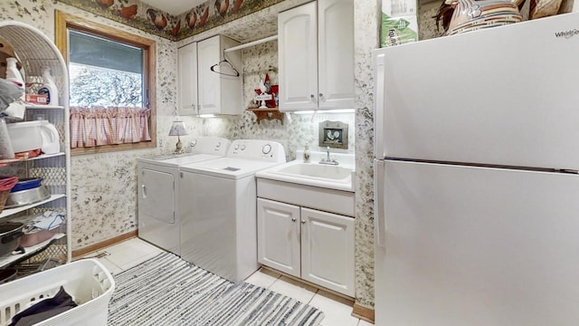 clothes washing area with sink, light tile patterned floors, washer and clothes dryer, and cabinets