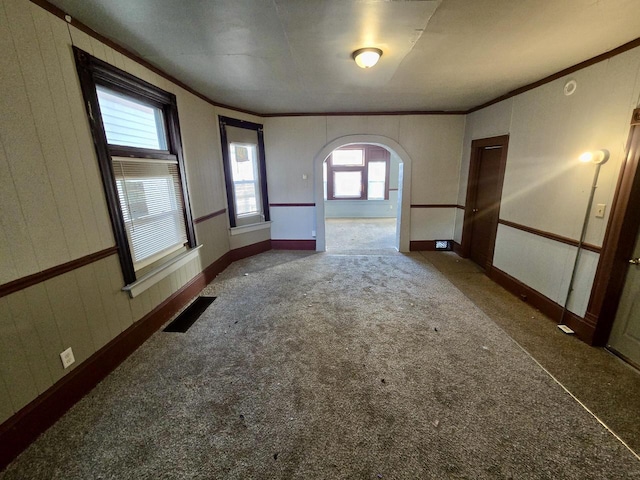 carpeted empty room featuring ornamental molding and wood walls