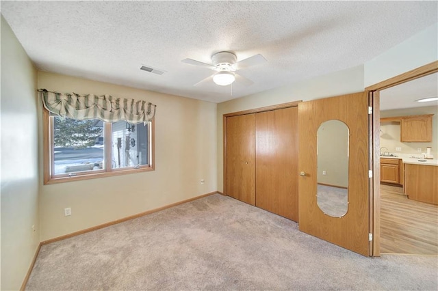 unfurnished bedroom featuring sink, ceiling fan, a textured ceiling, light colored carpet, and a closet