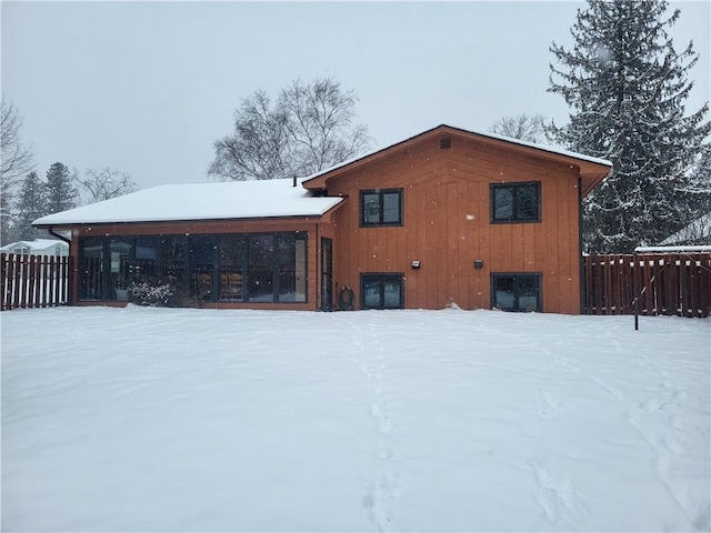 snow covered back of property featuring a sunroom