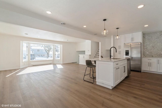 kitchen with appliances with stainless steel finishes, sink, white cabinets, hanging light fixtures, and a kitchen island with sink