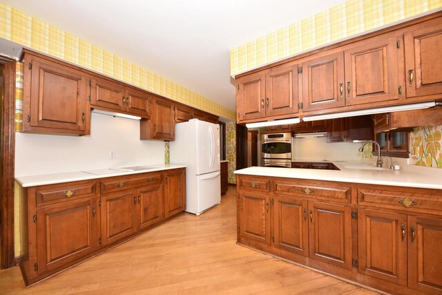 kitchen with white refrigerator, sink, double oven, and light hardwood / wood-style flooring