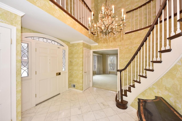 foyer featuring crown molding, a towering ceiling, a wealth of natural light, and an inviting chandelier