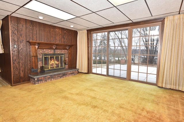 unfurnished living room featuring light colored carpet, a fireplace, a wealth of natural light, and wood walls