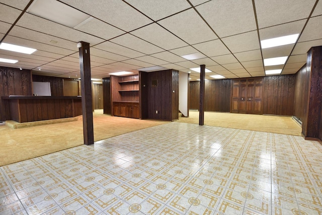 basement featuring light colored carpet, a paneled ceiling, and wood walls